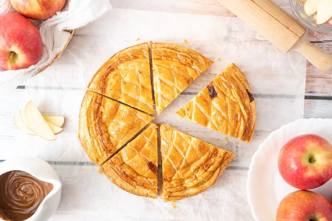 Galette des rois feuilletée dorée à la frangipane, posée à côté d'une couronne en papier